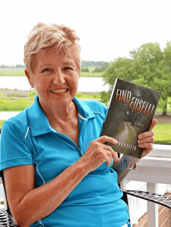 Elsa Bonstein on her porch, holding her first novel, Find Edsell!